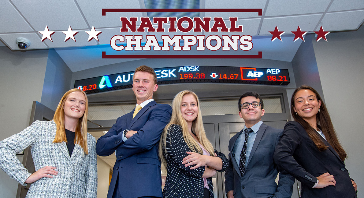 Students stand in Rehn Hall in front of ticker.