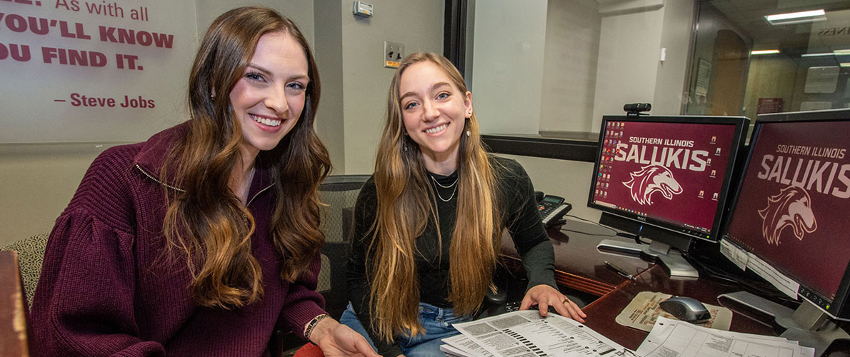two students smiling with IRS forms on the desk in front of them