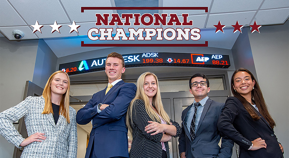 Students stand in Rehn Hall in front of ticker.